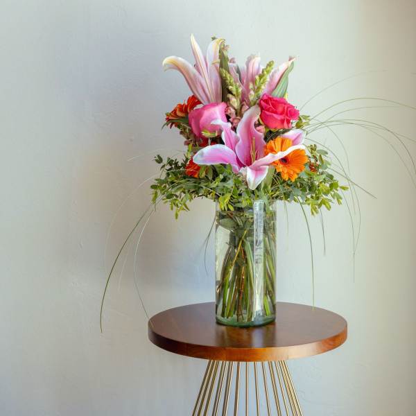 Tall bouquet of pink lilies and orange flowers in a glass vase
