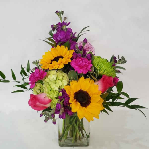 Mixed bouquet with sunflowers, roses, and purple blooms in a clear glass vase