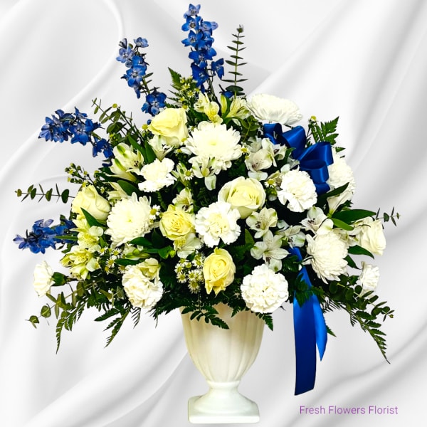 White and yellow floral arrangement with blue flowers in a white urn vase