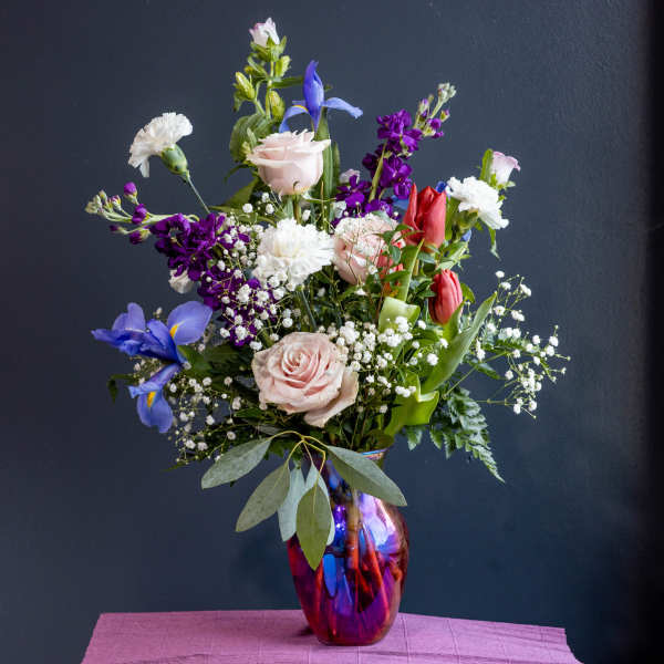 Mixed bouquet of roses, tulips, irises, and carnations in a glass vase
