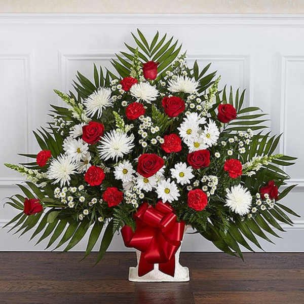 Fan-shaped red and white floral arrangement with roses and daisies in a white container with red bow