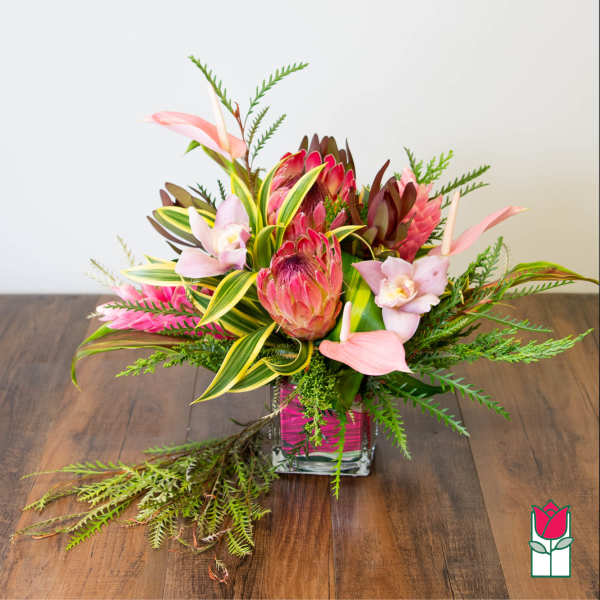 Tropical flower arrangement in a square glass vase with pink blooms
