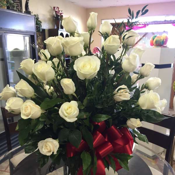 Bouquet of white roses in a clear glass vase with a red ribbon