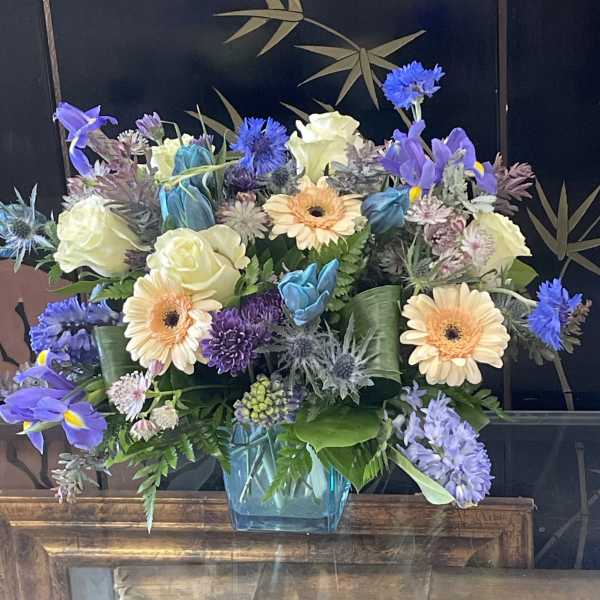 Mixed bouquet of blue, purple, and cream flowers in a glass vase