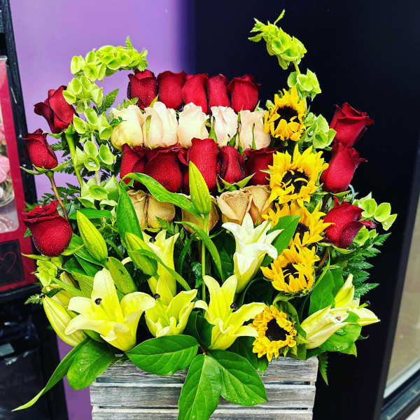 Mixed bouquet of red and cream roses with yellow lilies in a wooden box