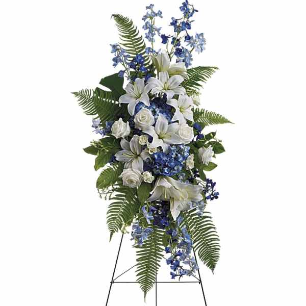 Tall standing spray of white lilies and roses with blue flowers on a metal easel