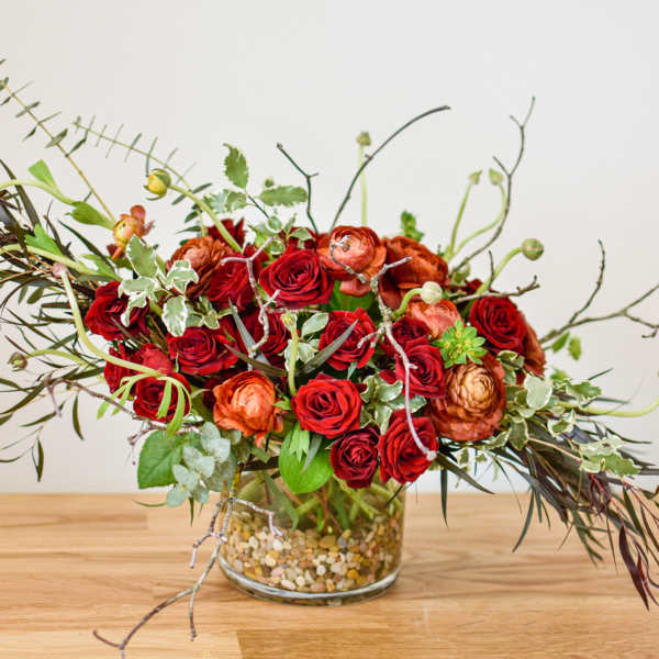 Red and orange rose arrangement in a glass vase with branches