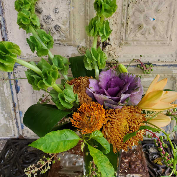 Bouquet with green bells of Ireland, purple cabbage, and orange blooms in a vase