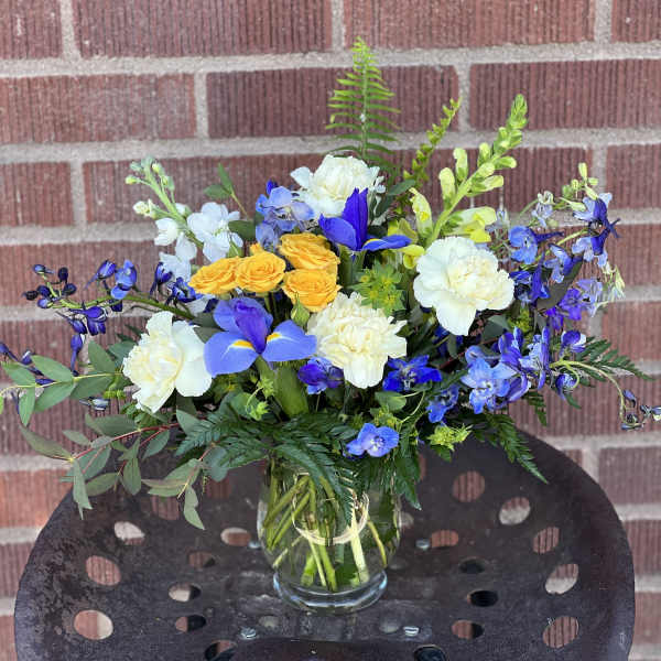 Mixed bouquet of blue, white, and yellow flowers in a glass vase