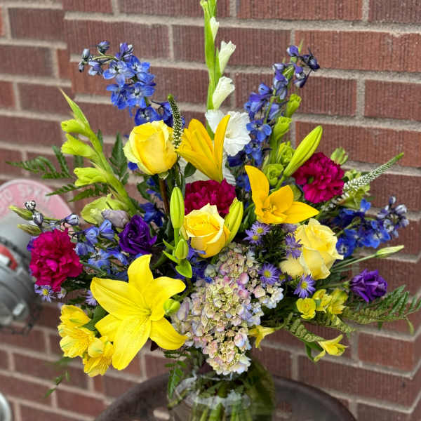 Mixed bouquet in a glass vase with yellow lilies, roses, and blue flowers