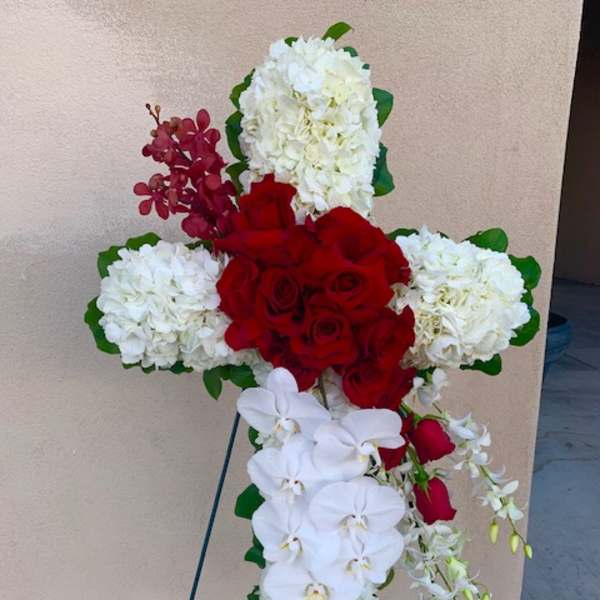 Cross-shaped floral tribute with red roses, white hydrangeas, and white orchids