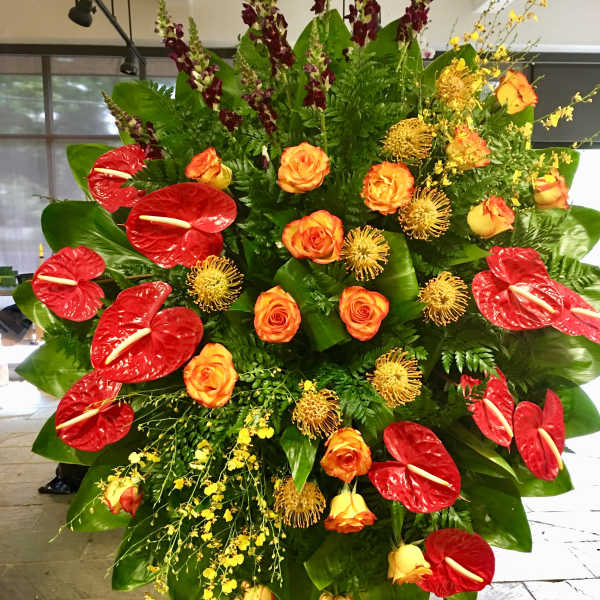 Large tropical floral standing arrangement with red anthuriums and orange roses