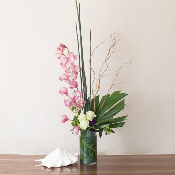 Tall modern arrangement with pink orchids and white roses in a clear cylinder vase