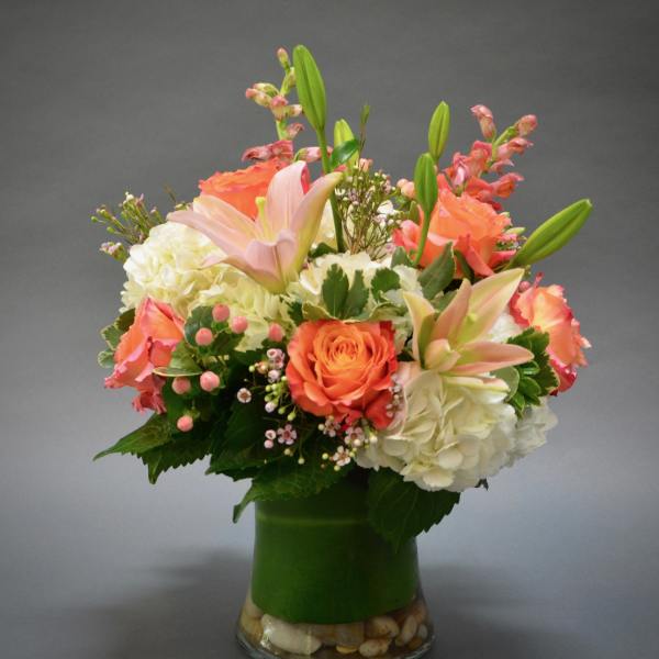Peach roses and lilies arranged with white hydrangeas in a glass vase