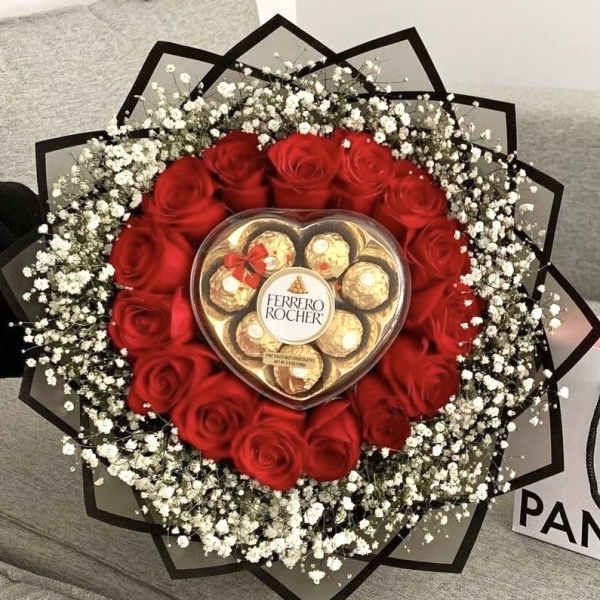 Round bouquet of red roses and white filler flowers with a heart box of chocolates in the center