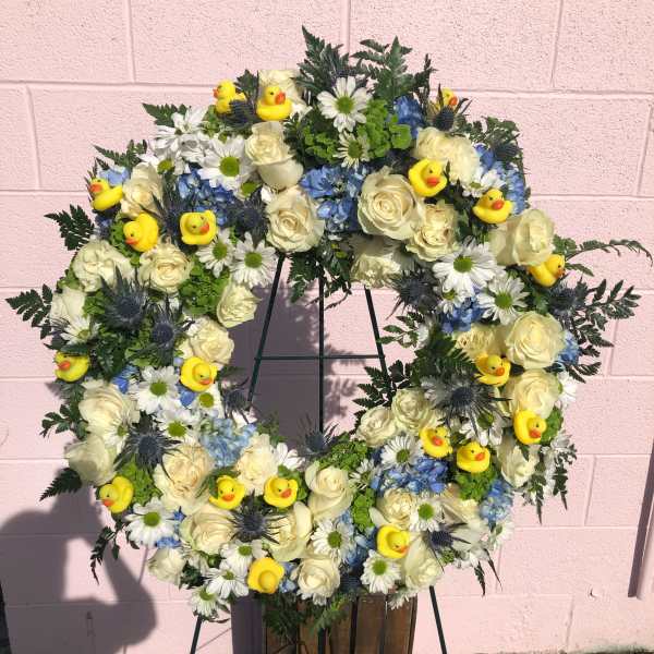 Wreath of white roses, blue flowers, and yellow duck decorations on a stand