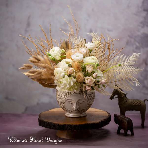 White floral arrangement in a decorative face vase with dried grasses