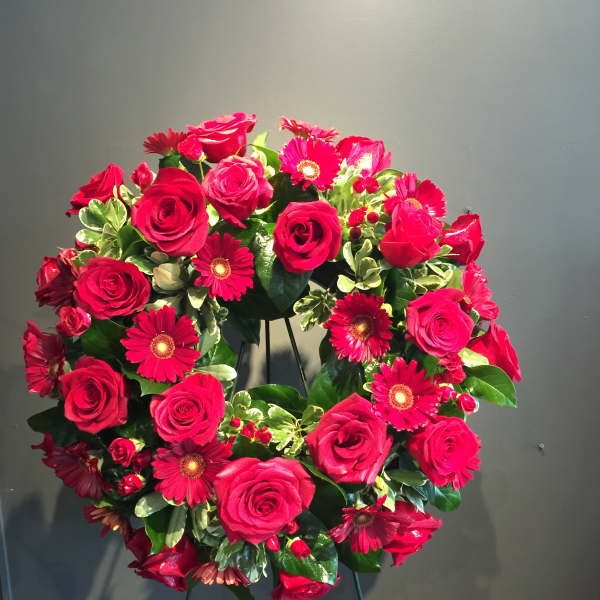 Heart-shaped wreath of red roses and pink daisies on a stand