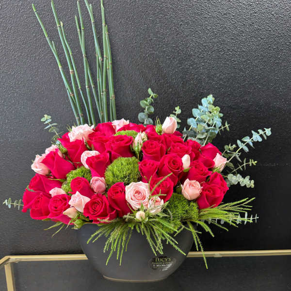 Pink and red roses arranged in a black vase with greenery