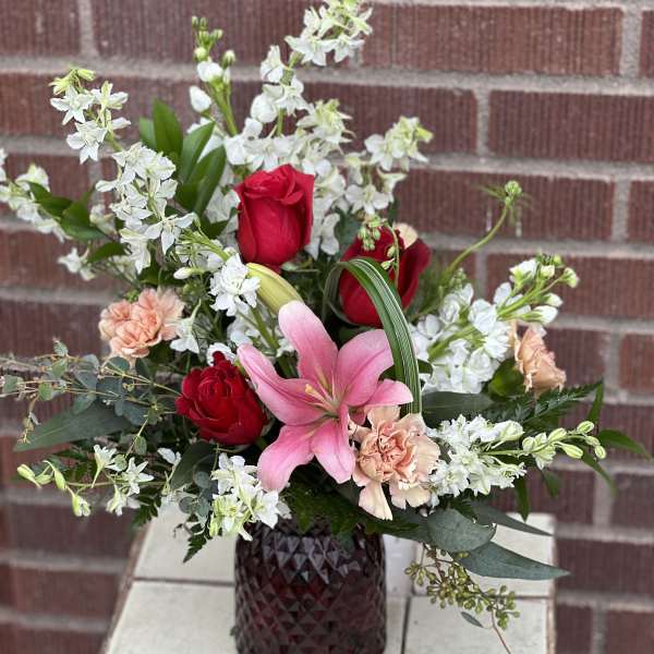 Pink lily and red roses in a dark glass vase