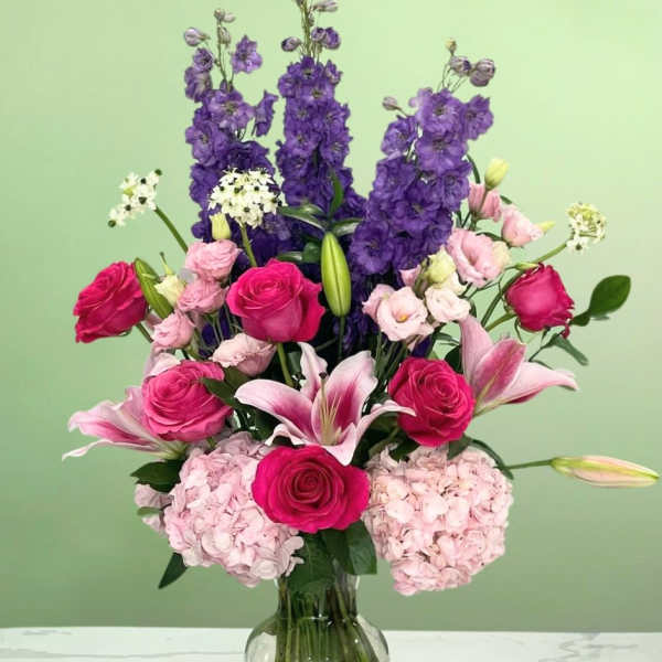 Pink roses and lilies in a glass vase with tall purple blooms