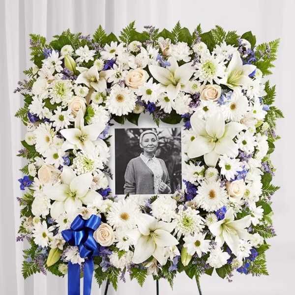 White floral funeral wreath with a photo in the center and blue ribbon