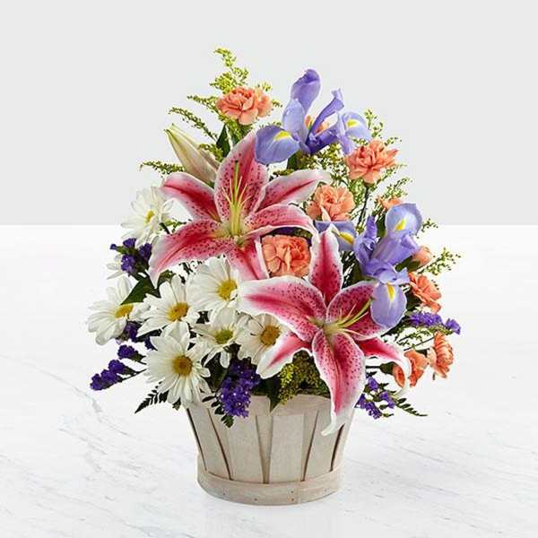 Mixed bouquet in a wooden basket with pink lilies, irises, daisies, and carnations
