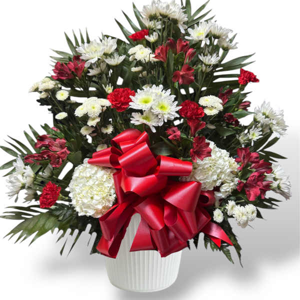 Red and white mixed flower arrangement in a white vase with a red bow