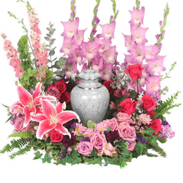 Cremation flower arrangement with pink gladiolus, lilies, and roses surrounding a gray urn