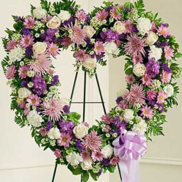 Heart-shaped standing wreath with purple, pink, and white flowers and a lavender ribbon bow
