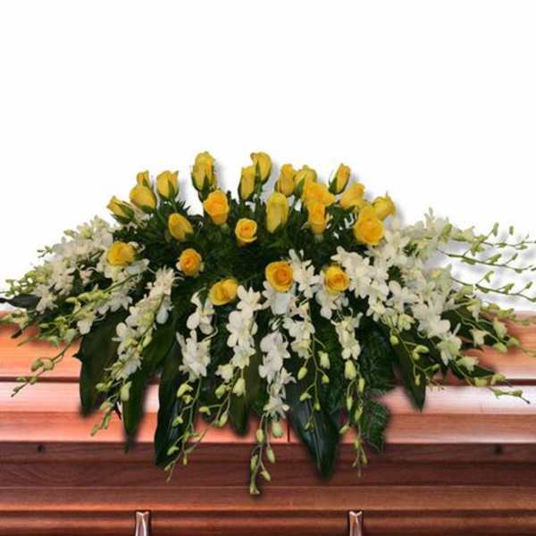 Yellow rose and white orchid casket spray arranged across a wooden casket