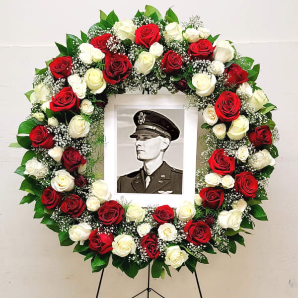 Standing circular wreath of red and white roses with baby’s breath framing a black-and-white portrait.
