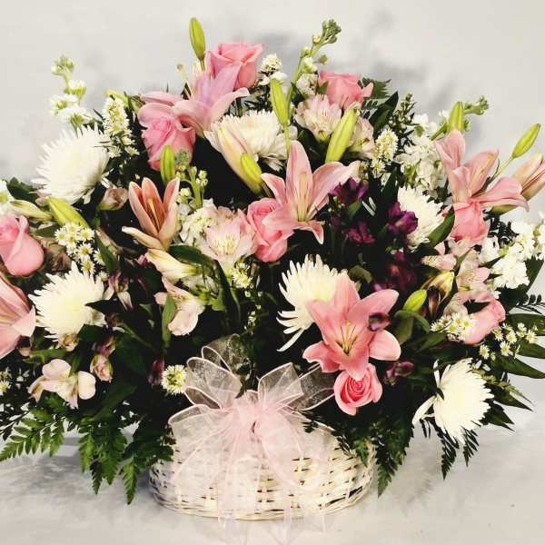 Pink lilies and roses in a white basket with a pink bow
