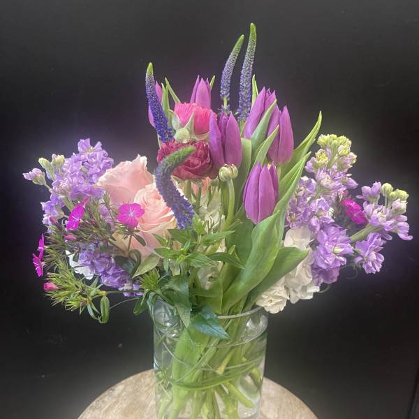 Mixed bouquet of purple tulips, pink roses, and lavender flowers in a glass vase