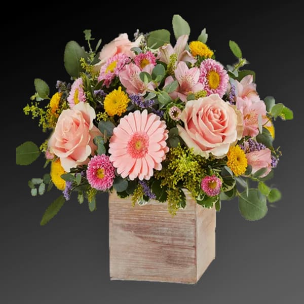 Pastel pink and yellow flower arrangement in a rustic wooden cube container