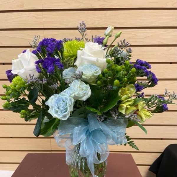 Bouquet of white and pale blue roses with purple filler in a glass vase