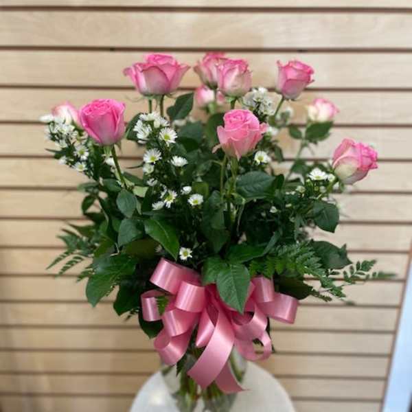 Pink roses arranged in a clear glass vase with a pink ribbon bow