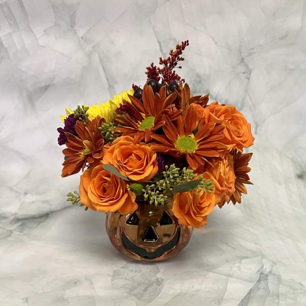 Orange roses and autumn-toned daisies in a pumpkin-shaped vase