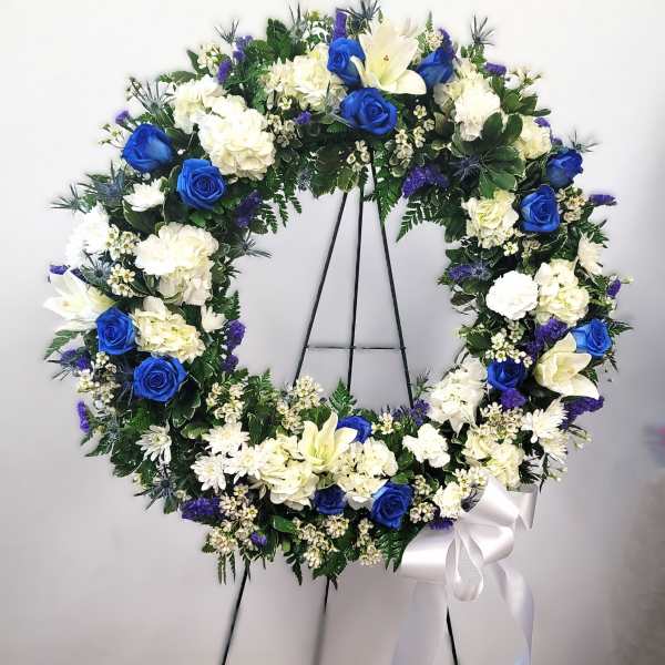 Blue and white floral wreath on a black stand with a white ribbon