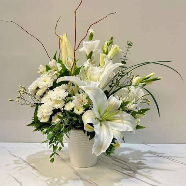 White lilies and small white flowers arranged in a white vase