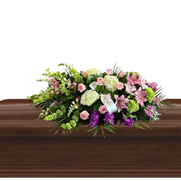 Pink and white floral casket spray on a wooden casket