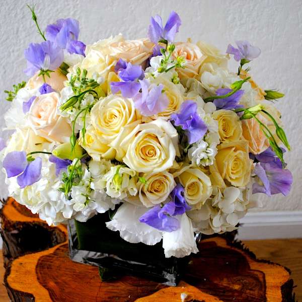 Bouquet of cream roses and purple flowers in a black vase