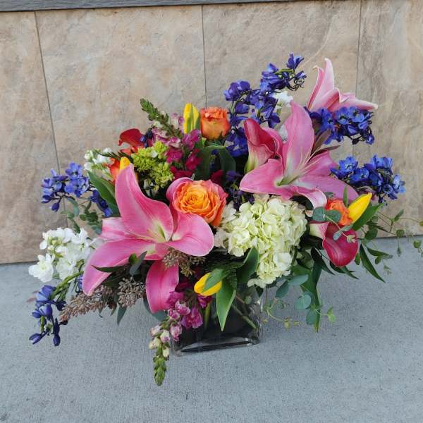 Mixed bouquet with pink lilies, roses, and blue flowers in a glass vase