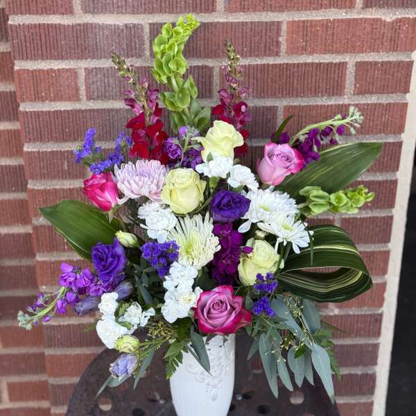 Mixed bouquet of roses, chrysanthemums, and purple flowers in a white vase