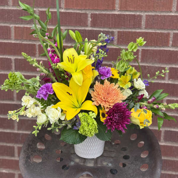Mixed bouquet with yellow lilies, purple blooms, and a white vase