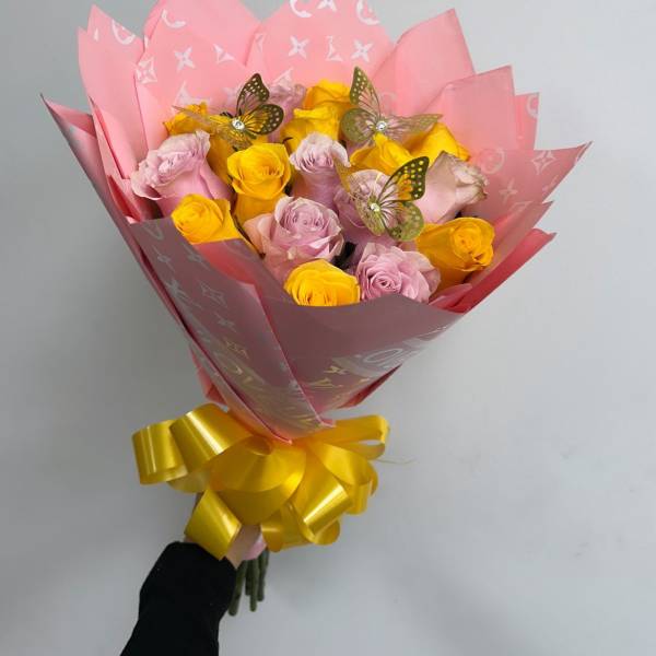 Bouquet of pink and yellow roses wrapped in pink paper with a yellow ribbon
