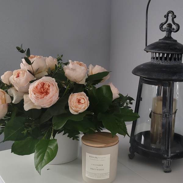 Peach roses in a white vase beside a black lantern and candle