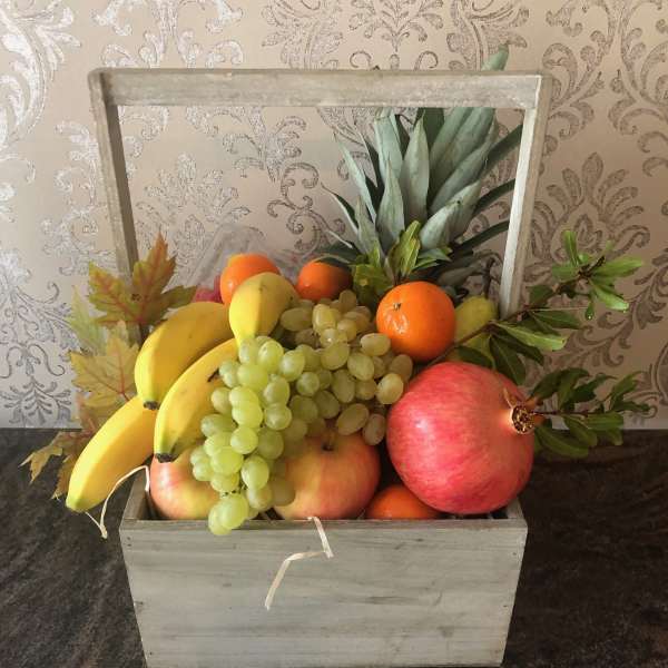 Wooden crate filled with assorted fruit including bananas, grapes, oranges, and pomegranates