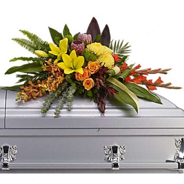 Floral spray on a silver casket with yellow and orange blooms