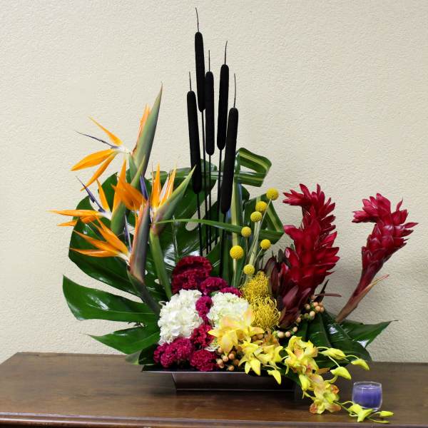 Tropical arrangement with red and orange flowers in a low rectangular vase